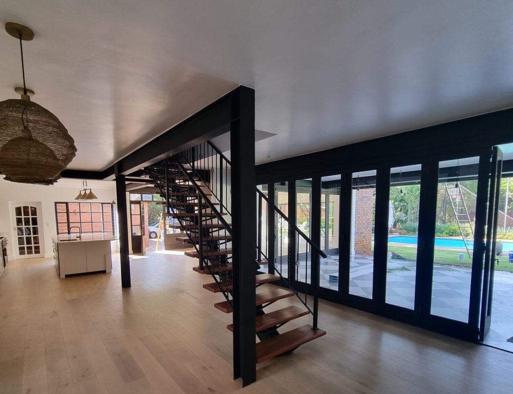 Open-plan interior showing the new staircase and dark-framed doors onto the garden and pool.