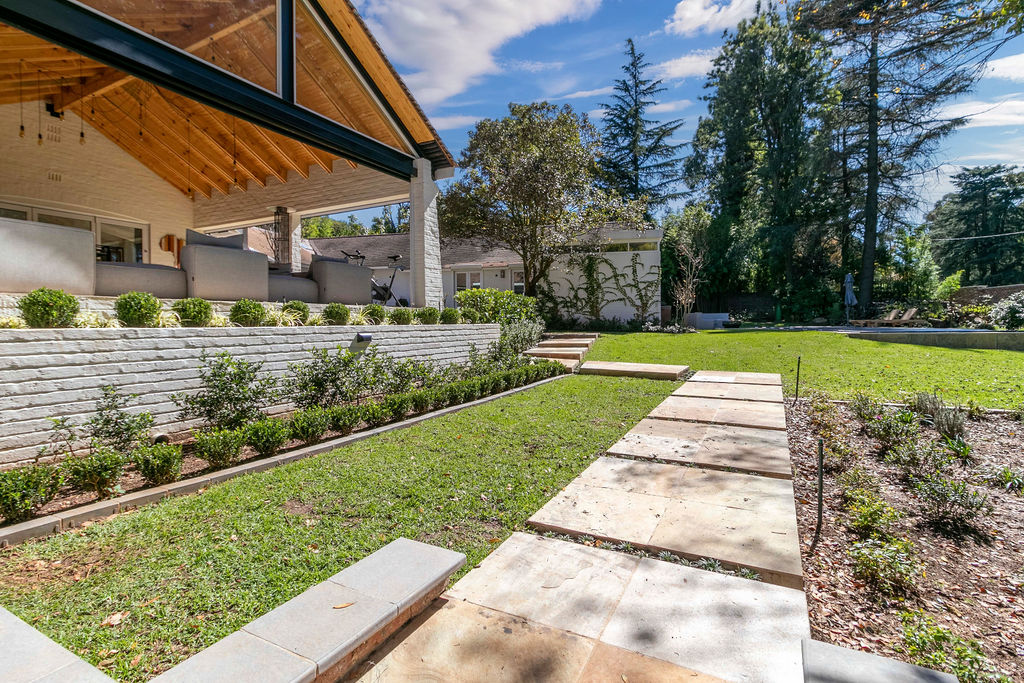 View of the covered patio with its timber ceiling, beside a stepped lawn and stone retaining wall.